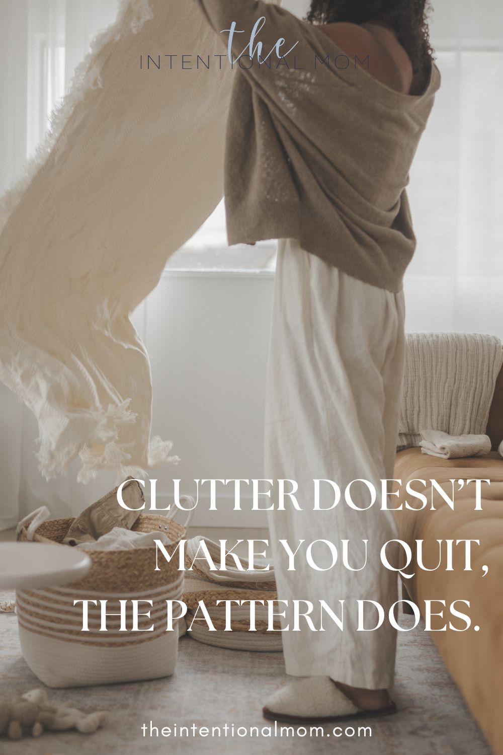 Person lifting a blanket in a calm living space with baskets and soft clutter nearby.